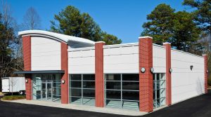 White commercial building with red brick columns, and a metal roof.