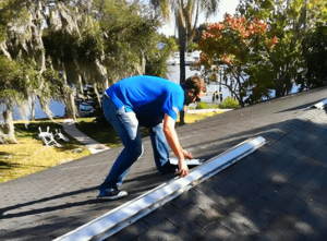 A man in a blue shirt working on top roof of a house. 